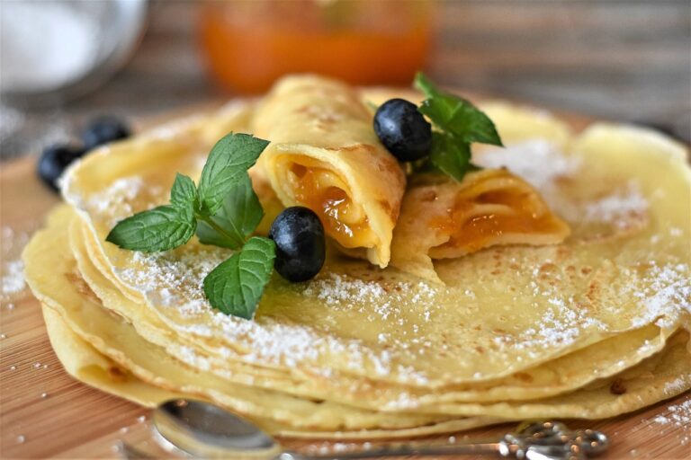 Pile de crêpes avec des bleuets et des crêpes rouler sur le dessus décoré avec des feuilles.